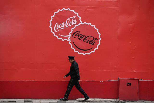 A security guard walks past a mural with the Coca-Cola logo in Mexico City on October 17, 2025. US giant Coca-Cola will reduce the sugar content of its soft drinks for the Mexican market by 30% after negotiating a new tax reduction on other products in its portfolio, the government of President Claudia Sheinbaum announced this Friday. (Photo by Yuri CORTEZ / AFP)