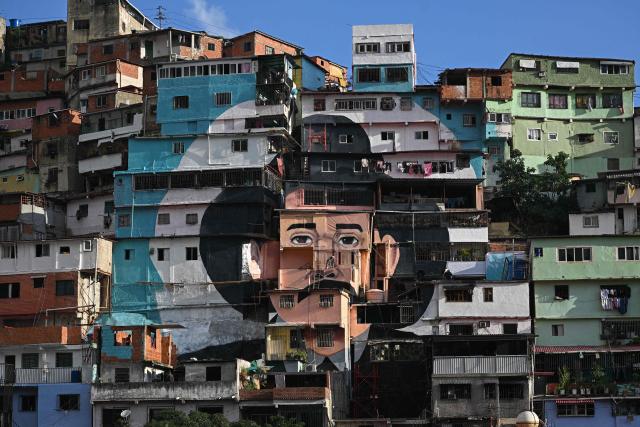 A man works in front of a giant mural of Venezuelan doctor Josй Gregorio Hernбndez, also known as "the doctor of the poor", painted across houses in the El Saman de Bolнvar community, in the Petare neighborhood of Caracas, on October 17, 2025. Pope Leo XIV is set to canonize Venezuela’s first saints, Dr. Jose Gregorio Hernandez and Sister Maria del Carmen Rendiles, during a ceremony in St. Peter's Square on October 19, 2025. (Photo by Federico PARRA / AFP)
