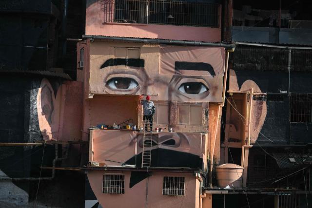 A man works in front of a giant mural of Venezuelan doctor Josй Gregorio Hernбndez, also known as "the doctor of the poor", painted across houses in the El Saman de Bolнvar community, in the Petare neighborhood of Caracas, on October 17, 2025. Pope Leo XIV is set to canonize Venezuela’s first saints, Dr. Jose Gregorio Hernandez and Sister Maria del Carmen Rendiles, during a ceremony in St. Peter's Square on October 19, 2025. (Photo by Federico PARRA / AFP)