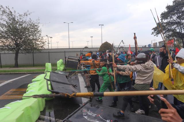 Demonstrators shoot arrows at police officers near the entrance of the US embassy during a protest in Bogota on October 17, 2025. Four police officers were injured by arrows and explosives on Friday during protests by social organizations outside the US Embassy in Bogota, rejecting the policies of the Donald Trump administration. (Photo by Andrea Ariza / AFP)