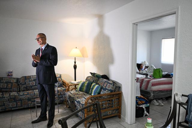 Ana Laura Ferrer Reina, 11, (R), daughter of Cuban dissident Jose Daniel Ferrer (L), looks at her phone as he speaks during an interview with AFP in their house in Miami, Florida, on October 16, 2025. There's no rest for Jose Daniel Ferrer, a Cuban dissident who arrived in the United States on October 13 and is determined to work with other exiles to democratically unseat the communist government in Havana. "We have to be proactive if we want to encourage Cubans to fight for their rights, for their freedom, instead of leaving the country with a 'save yourself if you can' type of mentality," the longtime activist told AFP from his new home in Miami. (Photo by CHANDAN KHANNA / AFP)