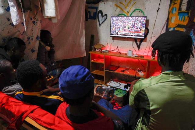 People watch the live broadcast of the public mourning in Kibera, Nairobi, on October 18, 2025 of Kenya’s opposition leader and former Prime Minister Raila Odinga taking place in Kisumu. Vast crowds gathered in Kisumu on October 18, 2025 to see the body of a beloved politician, Raila Odinga, for the biggest day of mourning ceremonies that have already claimed at least five lives. (Photo by SIMON MAINA / AFP)