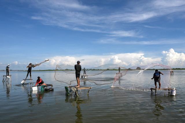 Cambodian men throw their fishing nets into a lake in Kandal province, near Phnom Penh, on October 18, 2025. (Photo by TANG CHHIN Sothy / AFP)