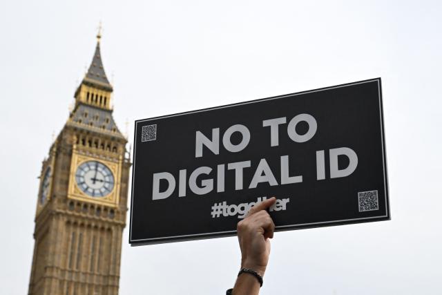 A demonstrator holds up a placard outside The Palace of Westminster during a march against the implementation of digital ID cards, in central London on October 18, 2025. UK Prime Minister Keir Starmer on September 26, 2025, announced plans for a new nationwide digital ID in a bid to curb illegal migration, but the move faces strong opposition in a country that has long resisted identity cards. The new digital ID will be held on people's phones and there will be no requirement for individuals to carry or be asked to produce it, the government said. A petition demanding that ID cards not be introduced has collected more than 2,889,412 signatures. (Photo by Chris J Ratcliffe / AFP)