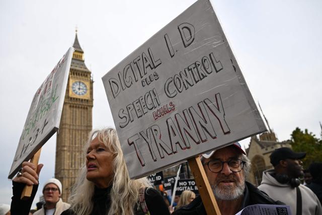 Demonstrators hold up placards outside The Palace of Westminster during a march against the implementation of digital ID cards, in central London on October 18, 2025. UK Prime Minister Keir Starmer on September 26, 2025, announced plans for a new nationwide digital ID in a bid to curb illegal migration, but the move faces strong opposition in a country that has long resisted identity cards. The new digital ID will be held on people's phones and there will be no requirement for individuals to carry or be asked to produce it, the government said. A petition demanding that ID cards not be introduced has collected more than 2,889,412 signatures. (Photo by Chris J Ratcliffe / AFP)