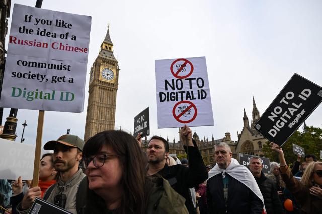 Demonstrators hold up placards outside The Palace of Westminster during a march against the implementation of digital ID cards, in central London on October 18, 2025. UK Prime Minister Keir Starmer on September 26, 2025, announced plans for a new nationwide digital ID in a bid to curb illegal migration, but the move faces strong opposition in a country that has long resisted identity cards. The new digital ID will be held on people's phones and there will be no requirement for individuals to carry or be asked to produce it, the government said. A petition demanding that ID cards not be introduced has collected more than 2,889,412 signatures. (Photo by Chris J Ratcliffe / AFP)