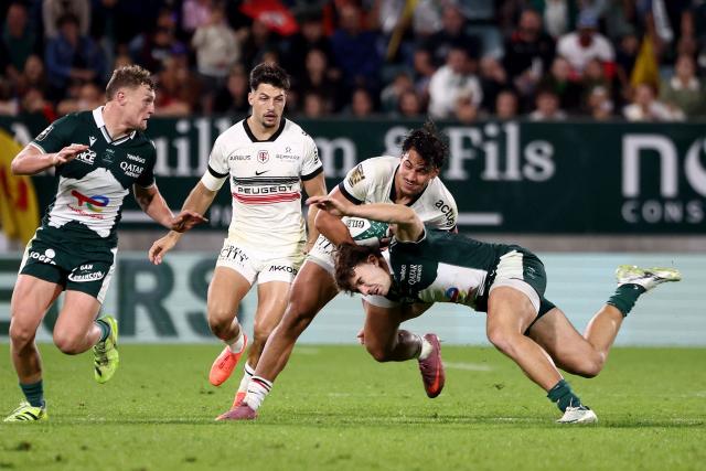 Toulouse's French centre Kalvin Gourgues (C) is tackled by Pau's French centre Fabien Brau-Boirie (bottom) during the French Top14 rugby union match between Section Paloise Bearn Pyrenees (Pau) and Stade Toulousain Rugby (Toulouse) at Stade du Hameau in Pau, south-western France on October 18, 2025. (Photo by ROMAIN PERROCHEAU / AFP)