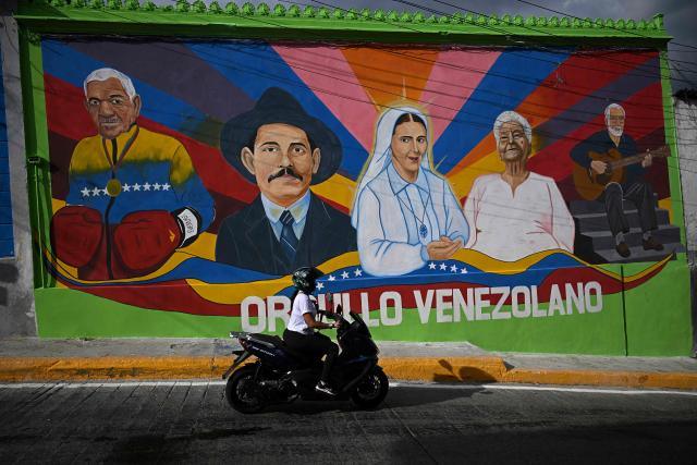 A motorbike rides past a mural depicting Venezuelan doctor Jose Gregorio Hernandez (2-L) and Venezuelan Sister Maria (C), on a street in the La Pastora neighborhood of Caracas, on October 18, 2025. Pope Leo XIV is set to canonize Venezuela’s first saints, Dr. Jose Gregorio Hernandez and Sister Maria del Carmen Rendiles, during a ceremony in St. Peter's Square on October 19, 2025. (Photo by Federico PARRA / AFP)
