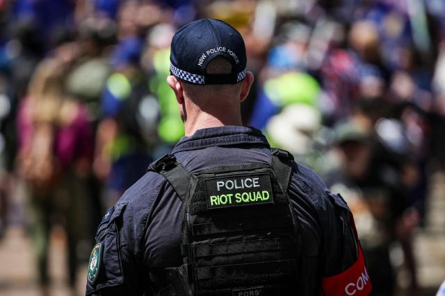 A New South Wales police riot squad officer walks towards protesters holding Australian national flags and banners as they participate in the March for Australia rally in central Sydney on October 19, 2025. (Photo by DAVID GRAY / AFP)