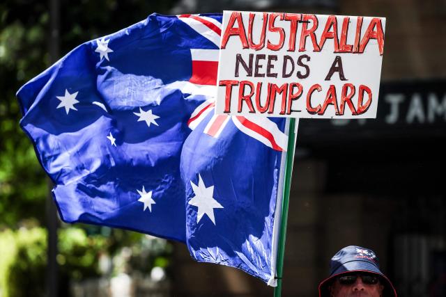 A protester holds a banner and an Australian national flag as he participates in the March for Australia rally in central Sydney on October 19, 2025. (Photo by DAVID GRAY / AFP)