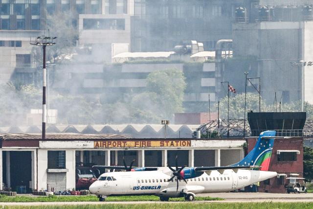 An aircraft prepares to take off as smoke rises from the fire-damaged cargo terminal of Hazrat Shahjalal International Airport, a day after the blaze in Dhaka on October 19, 2025. A large fire swept through the cargo terminal of Bangladesh's main international airport in Dhaka on October 18, forcing authorities to suspend all flights, officials said. (Photo by Munir UZ ZAMAN / AFP)