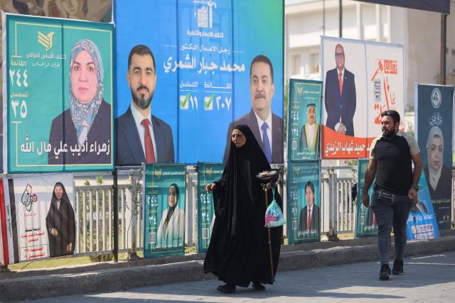 Iraqis walk past electoral billboards, including one bearing a portrait of Prime Minister Mohammed Shia al-Sudani (C), in central Baghdad on October 19, 2025, ahead of Iraq's parliamentary elections on November 11. (Photo by AHMAD AL-RUBAYE / AFP)