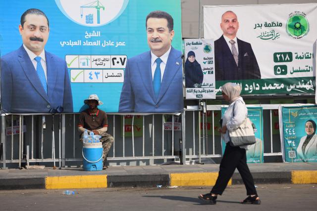A woman walks past electoral billboards, including one bearing a portrait of Prime Minister Mohammed Shia al-Sudani (C), in central Baghdad on October 19, 2025, ahead of Iraq's parliamentary elections on November 11. (Photo by AHMAD AL-RUBAYE / AFP)