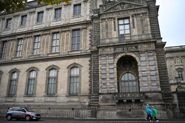 A police car is parked as people walk under the window from where entered the thieves who stole eight priceless royal pieces of jewellery from the Louvre Museum the day before, in Paris on October 20, 2025. The thieves arrived between shortly after the museum opened to the public at 9:00 am. They used a truck with an extendable ladder to get access to the Apollo Gallery, home to the royal collection, and cutting equipment to get in through a window and open the display cases. The Louvre will remain closed for a second day running on October 20. (Photo by JULIEN DE ROSA / AFP)