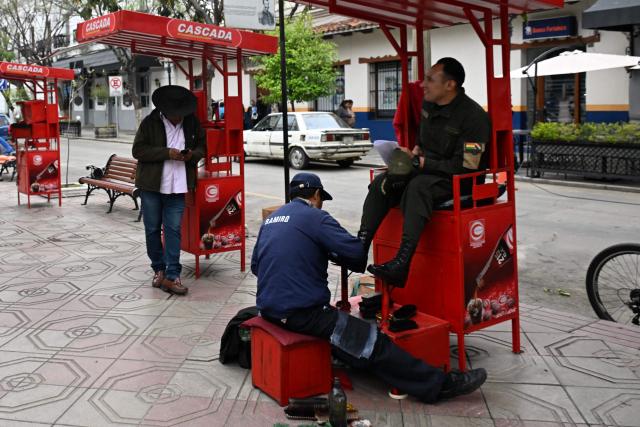 A shoe shiner polishes the boots of a Bolivian policeman the day after the presidential election runoff, in Tarija, Bolivia, on October 20, 2025. Bolivians on the eve elected pro-business center-right senator Rodrigo Paz as their new president, ending two decades of socialist rule that have left the South American nation deep in economic crisis. (Photo by AIZAR RALDES / AFP)