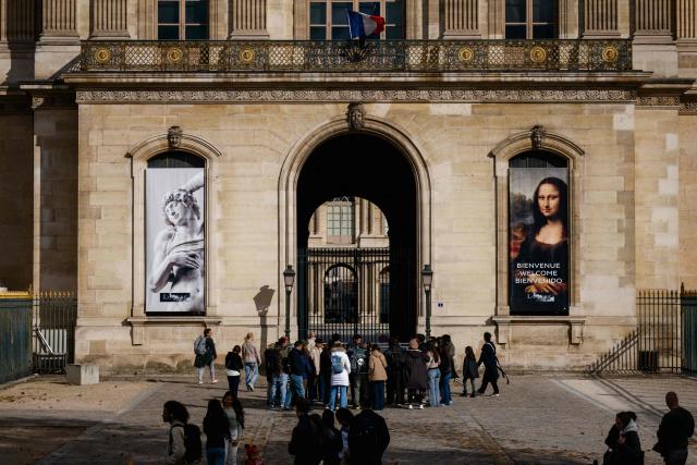 Tourists receive information from the tour guide in front of an entrance of the closed  Louvre pyramid courtyard after the announcement that the museum will remain closed for a second day following thieves stole priceless jewels from the museum in Paris a day earlier, in Paris on October 20, 2025. (Photo by Dimitar DILKOFF / AFP)