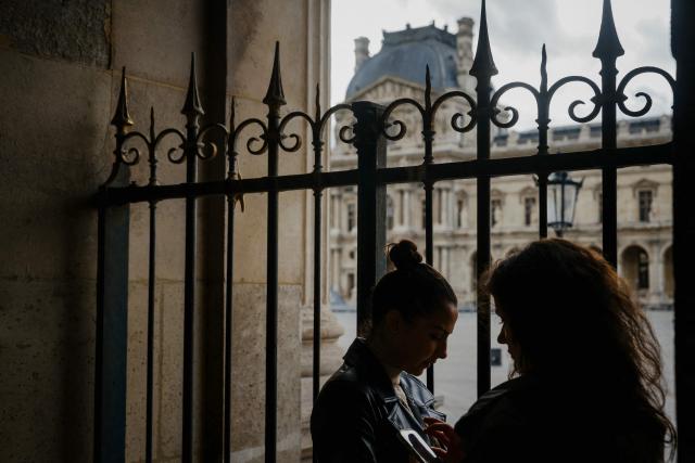 Tourists take photo withn their mobile phone to the Louvre pyramid courtyard after the announcement that the museum will remain closed for a second day following thieves stole priceless jewels from the museum in Paris a day earlier, in Paris on October 20, 2025. (Photo by Dimitar DILKOFF / AFP)