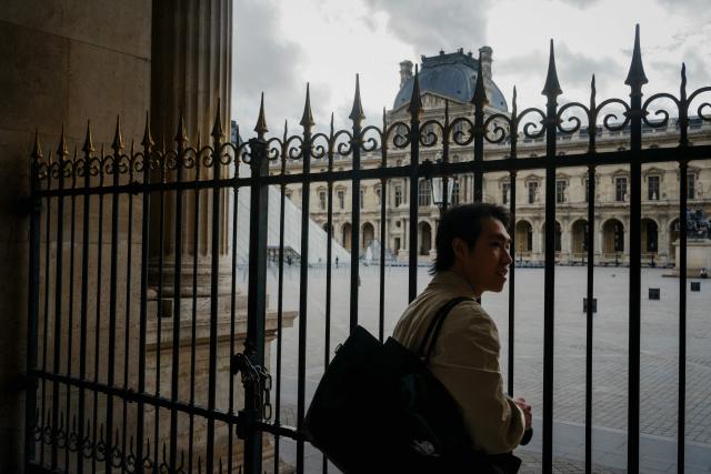 A tourist looks the Louvre pyramid courtyard through the closed gates after the announcement that the museum will remain closed for a second day following thieves stole priceless jewels from the museum in Paris a day earlier, in Paris on October 20, 2025. (Photo by Dimitar DILKOFF / AFP)