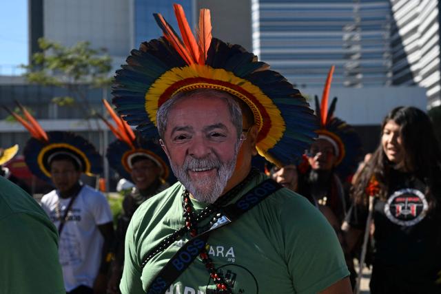 (FILES) A Manoki Indigenous man wears a mask of Brazil’s President Luiz Inacio Lula da Silva during a demonstration in front of the hotel where an oil blocks auction organized by Brazil's Oil and Gas Regulatory Agency (ANP) is taking place, in Rio de Janeiro, Brazil, on June 17, 2025. Just days before the COP30 climate summit in Brazil, Petrobras announced on October 20, 2025, that it had received authorization from environmental agency Ibama to begin oil drilling 500 km from the mouth of the Amazon River—a move that has sparked tensions between President Lula’s government and environmentalists. (Photo by Mauro PIMENTEL / AFP)