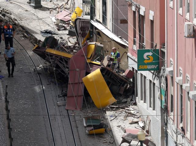 (FILES) Police and civil protection members work on the site of the Gloria funicular accident that killed 16 a day earlier in Lisbon, on September 4, 2025. An official inquiry called Monday for all Lisbon cable cars to be kept out of service for urgent modifications after a deadly crash in September that it blamed on a defective cable. The September 3 crash when the funicular came off the rails and hurtled into a building left 16 dead. The official inquiry's preliminary report said Lisbon's cable cars cannot resume operating until they can guarantee they have braking systems "capable of immobilizing the cabins in the event of a cable break." (Photo by PATRICIA DE MELO MOREIRA / AFP)