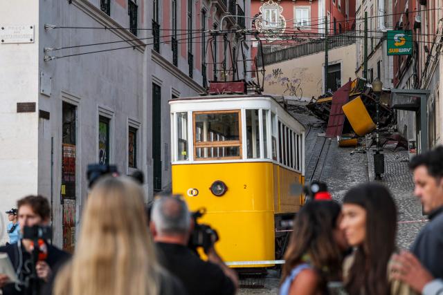 (FILES) Journalists work on the site of the Gloria funicular the day after an accident that killed 16 people a day earlier in Lisbon, on September 4, 2025. An official inquiry called Monday for all Lisbon cable cars to be kept out of service for urgent modifications after a deadly crash in September that it blamed on a defective cable. The September 3 crash when the funicular came off the rails and hurtled into a building left 16 dead. The official inquiry's preliminary report said Lisbon's cable cars cannot resume operating until they can guarantee they have braking systems "capable of immobilizing the cabins in the event of a cable break." (Photo by PATRICIA DE MELO MOREIRA / AFP)