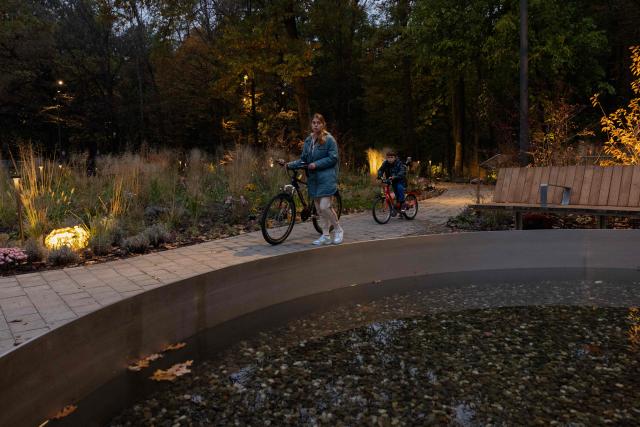 A woman and child push bicycles through a Therapeutic Garden in Kyiv, on October 20, 2025, amid the Russian invasion of Ukraine. Developed by artist and lighting designer Mykola Kabluka the Therapeutic Garden was created to assist in the recovery and emotional support of veterans and general public with the aim to restore health through movement in contact with nature. (Photo by Tetiana DZHAFAROVA / AFP)