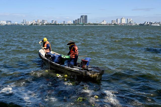 Workers on a boat collect trash in the water on West Lake in Hanoi on October 21, 2025. (Photo by Nhac NGUYEN / AFP)