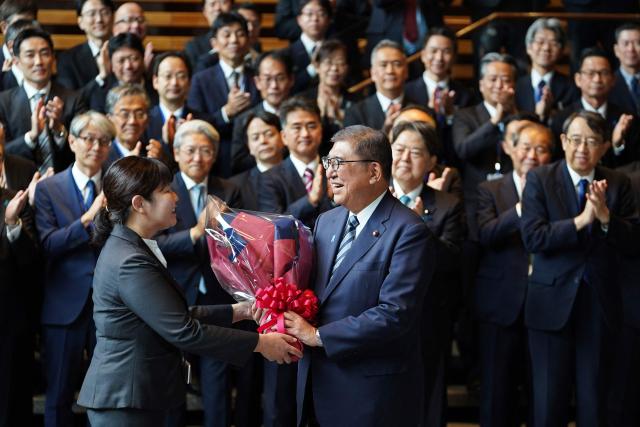 Japan's outgoing Prime Minister Shigeru Ishiba (centre R) receives flowers as he leaves the prime minister's office on his final day as the Japanese leader in Tokyo on October 21, 2025.  (Photo by Kazuhiro NOGI / AFP)