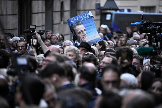 TOPSHOT - Supporters of France's former president Nicolas Sarkozy gather outside his residence ahead of his departure to La Sante prison for incarceration on a five-year prison sentence, after being convicted of criminal conspiracy over a plan for late Libyan dictator Moamer Kadhafi to fund his 2007 electoral campaign, in Paris, on October 21, 2025. Nicolas Sarkozy, who has faced a flurry of legal woes since losing re-election in 2012, is to be jailed on October 21, 2025, over a scheme to acquire Libyan funding for his successful 2007 presidential run, becoming the first former head of a European Union country to serve time behind bars. The former French right-wing leader has appealed the verdict and denounced an "injustice". (Photo by JULIEN DE ROSA / AFP)
