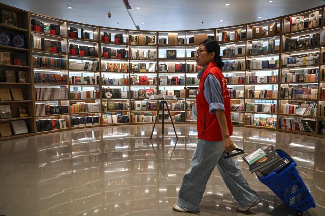 A staff member of a bookstore walks past book shelves at a bookstore in Shenzhen, in southern China's Guangdong province on October 21, 2025. (Photo by Jade GAO / AFP)