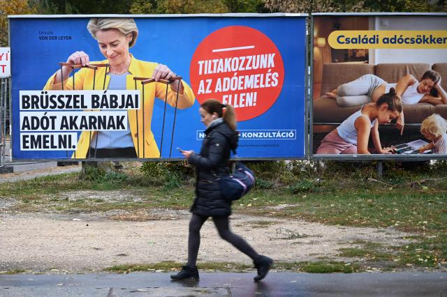 A woman walks in front of Hungarian goverment billboard depicting EU President Ursula von der Leyen as a puppet master reading "Brussels' puppets want to raise  taxes", in Budapest, on October 21, 2025. (Photo by Attila KISBENEDEK / AFP)