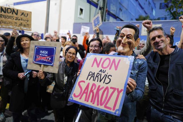 A local resident, wearing a mask of Nicolas Sarkozy, holds a placard protesting against the mayor of Nice's proposal to name the square in front of the future police station after former French President Nicolas Sarkozy, in Nice on october 21, 2025. France's fomer President Nicolas Sarkozy became the first former head of an EU state to be jailed on October 21, 2025, proclaiming his innocence as he entered a Paris prison. (Photo by Valery HACHE / AFP)