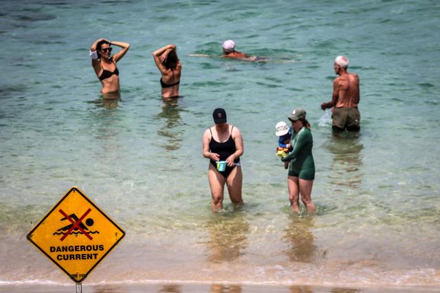 People swim in front of a warning sign on a hot and windy spring day at Sydney’s Bondi Beach on October 22, 2025. (Photo by DAVID GRAY / AFP)
