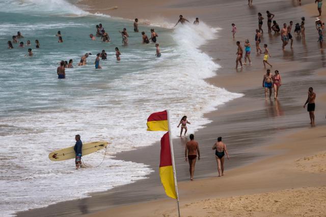 People swim and walk along Bondi Beach on a hot and windy spring day in Sydney on October 22, 2025. (Photo by DAVID GRAY / AFP)