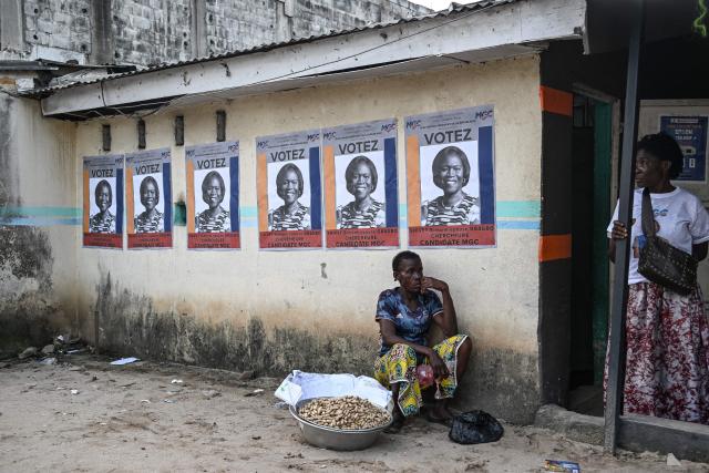 A grain seller sits near campaign posters of former Ivorian First Lady and presidential candidate for the Movement of the Capable Generations (MGC), Simone Ehivet Gbagbo, before her arrival for a campaign rally at Le Barron, in the working-class commune of Yopougon in Abidjan on October 22, 2025. The presidential election is scheduled for October 25, 2025. (Photo by Sia KAMBOU / AFP)