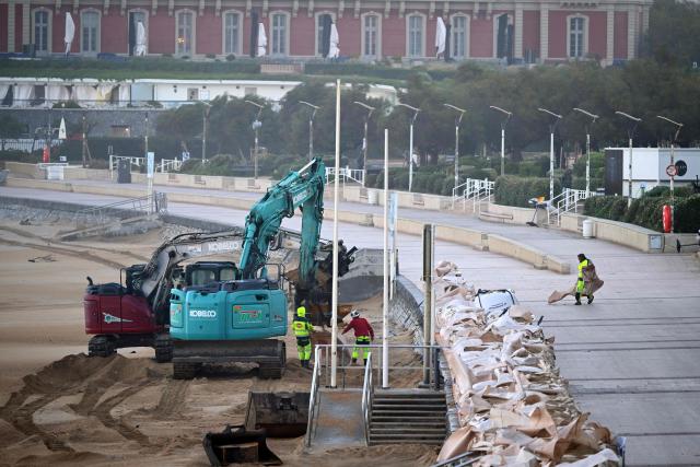 Mechanical shovels lay bags full of sand to protect the promenade of the 'Grande Plage', in Biarritz, south-western France on October 23, 2025. Winds gusted at over 100 km/h across much of France on October 23, 2025 morning as autumn storm Benjamin swept through the country. Meteo France classified the storm as "severe" and issued an orange alert for 19 departments. (Photo by Gaizka IROZ / AFP)