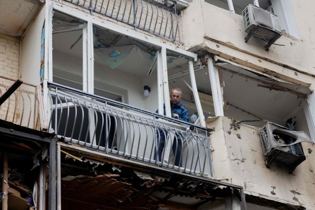 A man stands on the balcony of a damaged residential building with broken windows following a drone attack in Kyiv, on October 23, 2025, amid the Russian invasion of Ukraine. (Photo by Tetiana DZHAFAROVA / AFP)