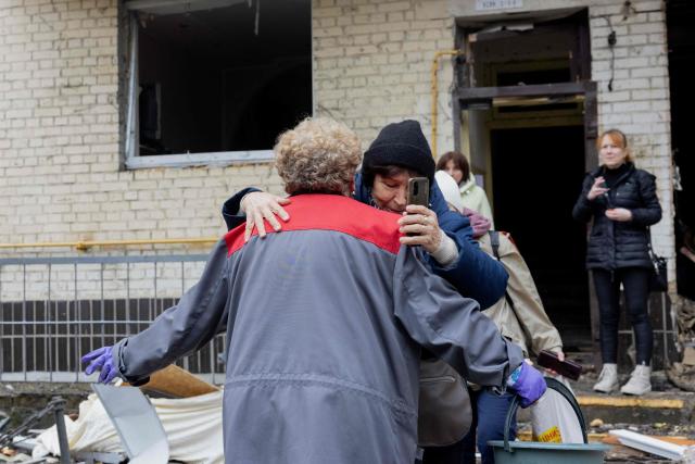 Women hug near a damaged residential building following a drone attack in Kyiv, on October 23, 2025, amid the Russian invasion of Ukraine. (Photo by Tetiana DZHAFAROVA / AFP)