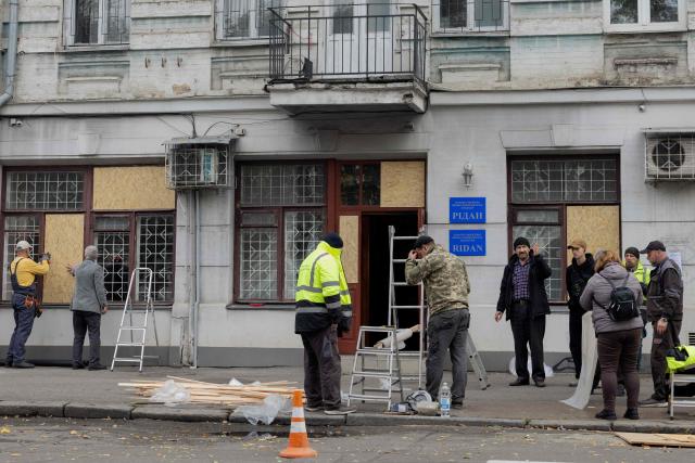 People cover broken windows with plywood panels after a drone attack in Kyiv, on October 23, 2025, amid the Russian invasion of Ukraine. (Photo by Tetiana DZHAFAROVA / AFP)