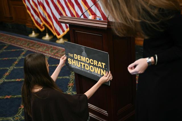 Aides set up signage before the start of a news conference with Speaker of the House Mike Johnson, Republican from Louisiana, at the US Capitol in Washington, DC, on October 23, 2025. The US government shutdown entered its fourth week Wednesday, becoming the second longest in history, as Donald Trump's Republicans and the opposition Democrats faced increasing pressure to end a stalemate that has crippled public services. Federal workers are set to miss their first full paychecks in the coming days, including tens of thousands of air traffic controllers and airport security agents -- an inflection point that helped end the last shutdown in 2019. (Photo by Brendan SMIALOWSKI / AFP)