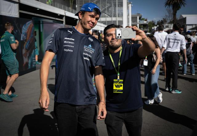 Williams' Thai driver Alexander Albon (L) poses for a selfie with a fan as they walk on the paddock ahead of the Mexico City Formula One Grand Prix at the Hermanos Rodriguez racetrack in Mexico City on October 23, 2025. (Photo by Carl DE SOUZA / AFP)