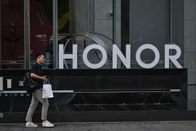 This photo taken on October 21, 2025 shows a man walking past the logo of Chinese smartphone company Honor at its headquarter in Shenzhen, in southern China's Guangdong province. (Photo by Jade GAO / AFP)