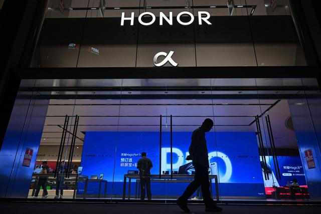 This photo taken on October 21, 2025 shows a man walking past an Honor retail store in Shenzhen, in southern China's Guangdong province. (Photo by Jade GAO / AFP)