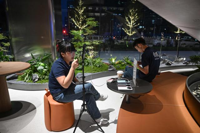 This photo taken on October 21, 2025 shows an employee (L) introducing Honor Magic 8 smartphones during a livestream at an Honor retail store in Shenzhen, in southern China's Guangdong province. (Photo by Jade GAO / AFP)