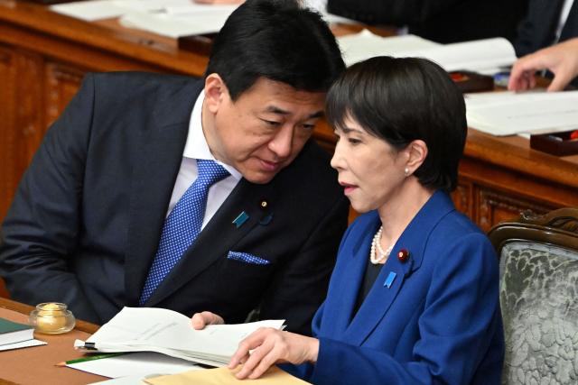 Japan's Prime Minister Sanae Takaichi (R) chats with Chief Cabinet Secretary Minoru Kihara after delivering her policy speech in the House of Representatives plenary session in Tokyo on October 24, 2025. Japan's new prime minister Sanae Takaichi said on October 24 she would try to achieve the country's target of spending two percent of GDP on defence two years early. (Photo by Kazuhiro NOGI / AFP)