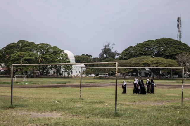 Schoolgirls walk in the grounds where a campaign rally of the ruling Tanzanian Chama Cha Mapinduzi (CCM - Revolutionary Party) of the incumbent President Samia Suluhu Hassan is scheduled to happen in Stone Town, on October 24, 2025. (Photo by MARCO LONGARI / AFP)
