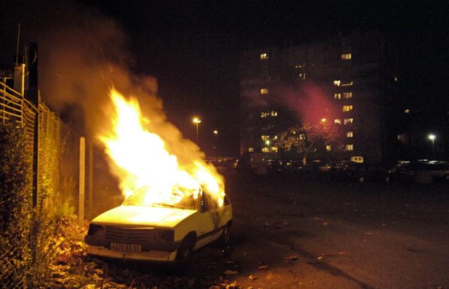 (FILES) A car is burning, 05 November 2005 in the Cite de l'Europe neighborhood in Aulnay-sous-Bois, a northern surburb of Paris, on the tenth straight night of unrest following the death by electrocution of two boys, last 27 October, who believed they were chased by police. On October 27, 2005, Zyed Benna and Bouna Traore, aged 17 and 15, died from electrocution in an EDF power substation where they had taken refuge after being chased by the police. This tragedy sparked a series of riots that spread from Clichy-sous-Bois to the rest of the country for three weeks, leading to the declaration of a state of emergency. (Photo by STEPHANE DE SAKUTIN / AFP)