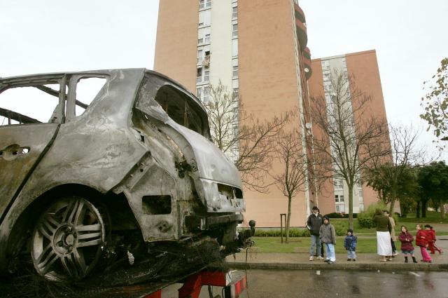 (FILES) A car is being towed at the Maurice Thorez neighborhood as residents look on, 04 November 2005 in Trappes. On October 27, 2005, Zyed Benna and Bouna Traore, aged 17 and 15, died from electrocution in an EDF power substation where they had taken refuge after being chased by the police. This tragedy sparked a series of riots that spread from Clichy-sous-Bois to the rest of the country for three weeks, leading to the declaration of a state of emergency. (Photo by Mehdi FEDOUACH / AFP)