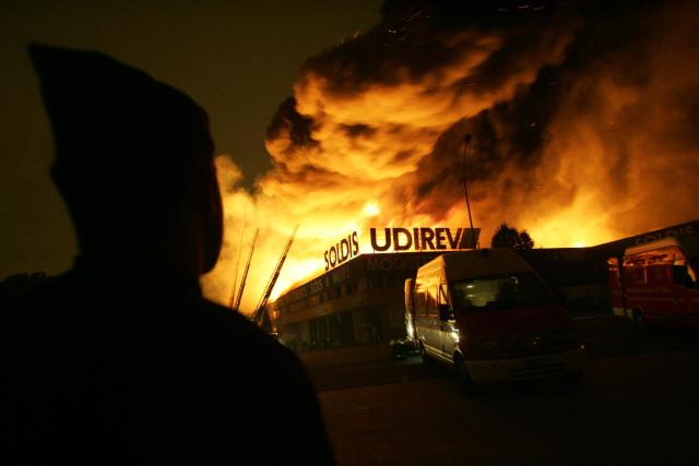 (FILES) A policeman look as firefighters extinguish a warehouse set ablaze in the early hours of 04 November 2005 in Aulnay-sous-Bois on the seventh consecutive night of violence on the ouskirts of the French capital. On October 27, 2005, Zyed Benna and Bouna Traore, aged 17 and 15, died from electrocution in an EDF power substation where they had taken refuge after being chased by the police. This tragedy sparked a series of riots that spread from Clichy-sous-Bois to the rest of the country for three weeks, leading to the declaration of a state of emergency. (Photo by Thomas COEX / AFP)
