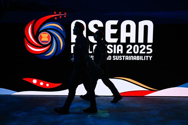 Members of the Royal Malaysia Police walk next to the Association of Southeast Asian Nations (ASEAN) logo ahead of the 47th ASEAN Summit in Kuala Lumpur on October 25, 2025. US President Donald Trump arrives in Malaysia on October 26 for the Association of Southeast Asian Nations (ASEAN) summit -- a meeting he skipped several times in his first term. (Photo by Mohd RASFAN / AFP)